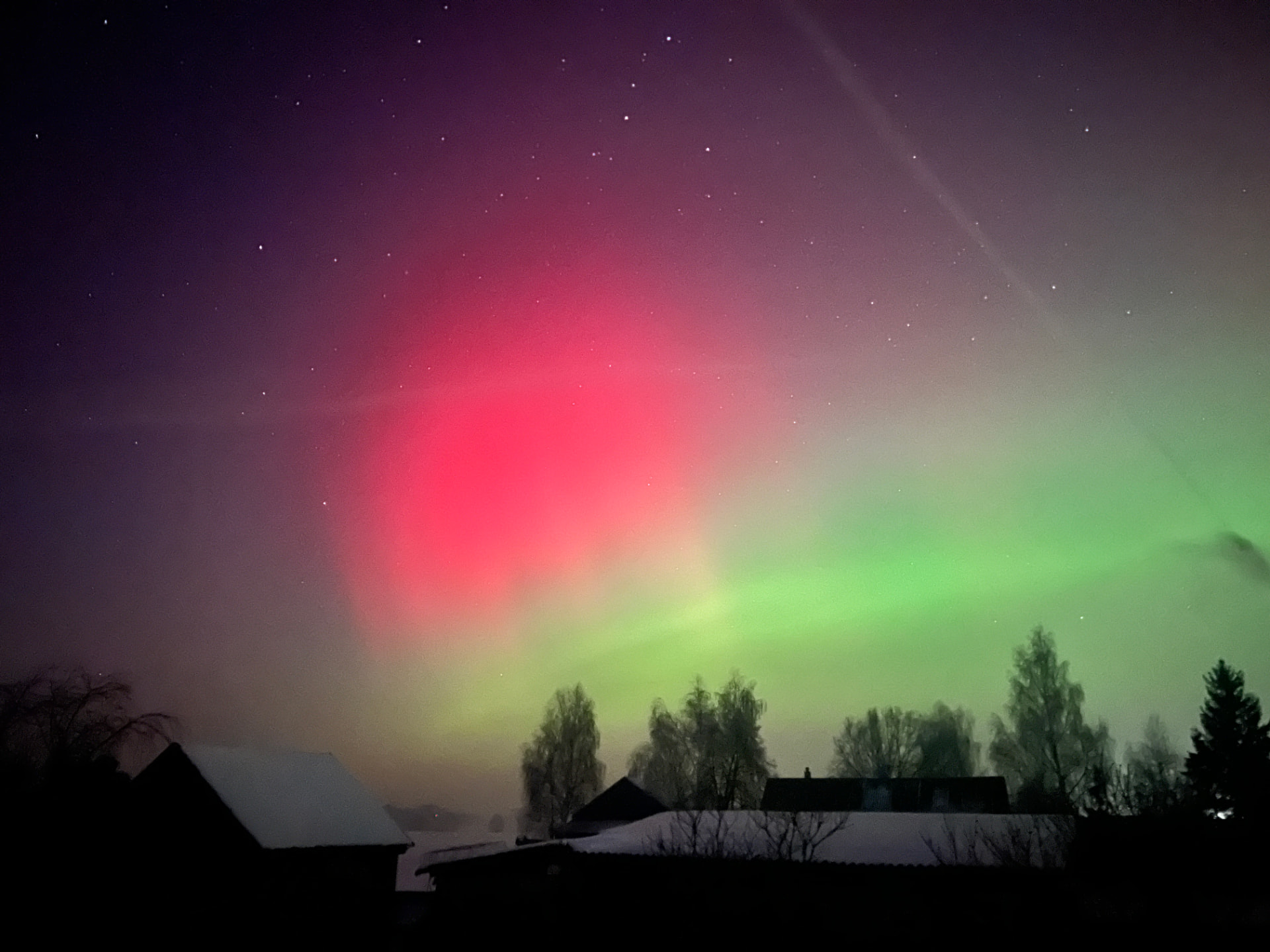Zorza polarna nad zaśnieżoną wsią — nocne niebo w czerwieniach i zieleniach